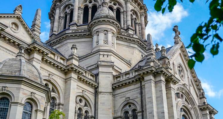 Gros plan des détails en pierre ornementée et de la tour en dôme d'une église historique contre un ciel bleu avec un cadre de feuillage.