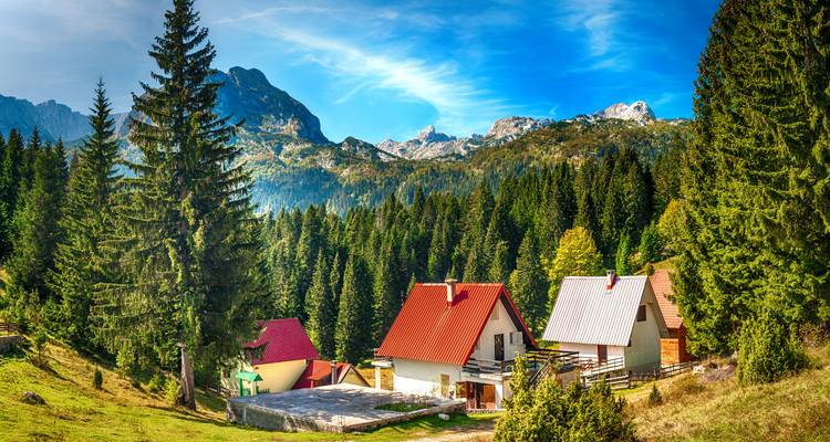 Malerische Almhütten mit roten Dächern eingebettet in Nadelwälder unterhalb der schroffen Gipfel des Durmitor.