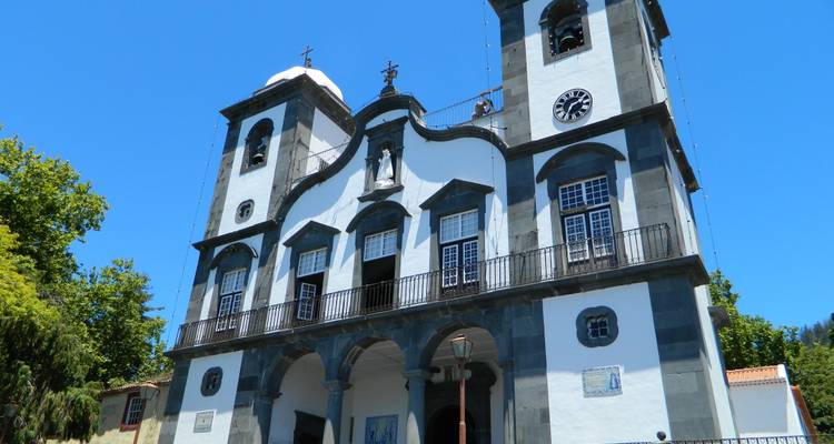 Een witte en grijze stenen kerk met twee torens en een wijzerplaat steekt af tegen een diepblauwe lucht.