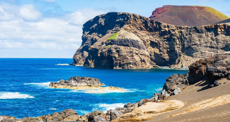 Dramatic volcanic sea cliffs with layered rock rising above deep blue Atlantic waters.