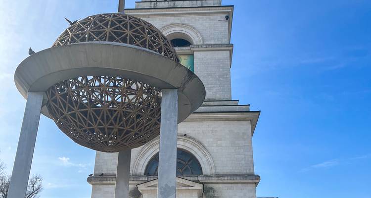 Moderne rasterbol sculptuur voor een witte stenen klokkentoren tegen een blauwe hemel.