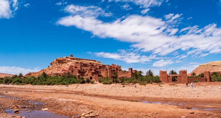 Le village forteresse de l'UNESCO d'Ait Benhaddou s'élève au-dessus d'un lit de rivière asséché sous un ciel bleu vif parsemé de nuages épars.