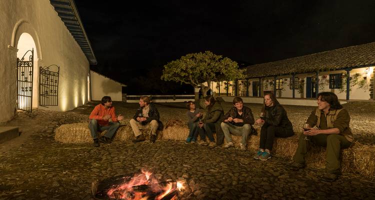 Gruppe von Freunden, die auf Heuballen um ein Lagerfeuer in einem gepflasterten Innenhof bei Nacht sitzen.