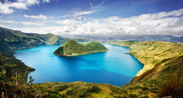 Panoramablick auf den türkisfarbenen Kratersee Cuicocha mit einer üppig grünen Insel in der Mitte, umgeben von Andenhügeln.