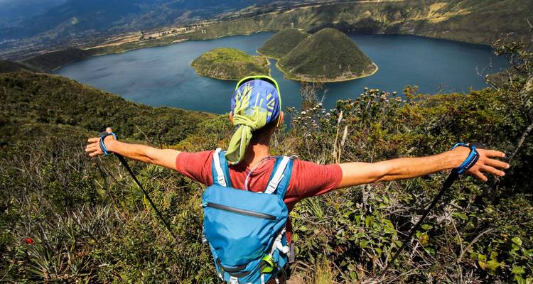 Rucksacktourist mit ausgestreckten Armen genießt einen hohen Aussichtspunkt über den Cuicocha-See und seine Inseln.