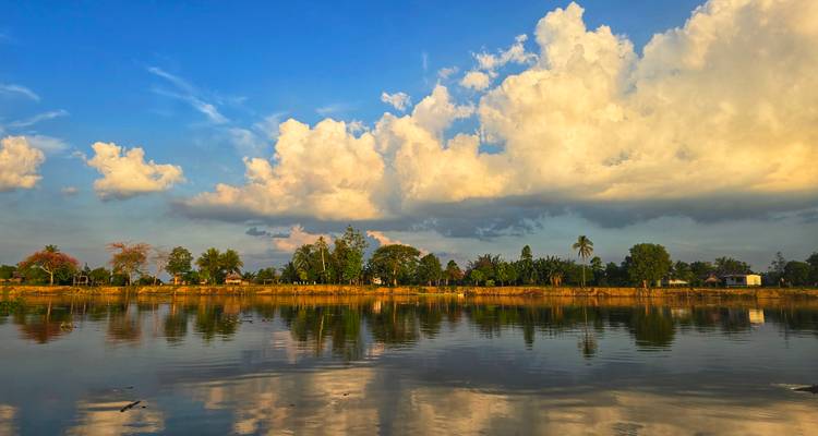 Het gouden uur licht werpt warme wolken en bomen in perfecte reflectie op een brede kalme rivier.