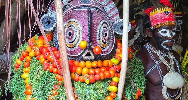 Tribale performer die een levendige tomaat- en bladerenkraag en gebeeldhouwd masker draagt, bereidt zich voor op ceremonie.