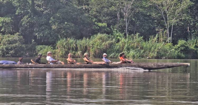 Lange houten kano met verschillende reizigers die peddelen langs een rustige junglerivier