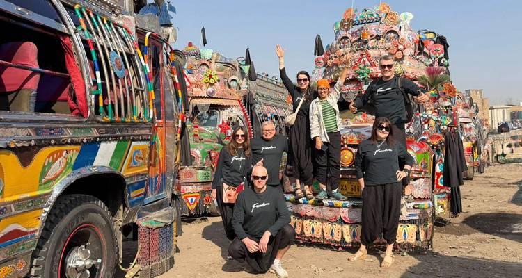 Un groupe de touristes se tient parmi des camions pakistanais aux couleurs vives dans une cour de camions colorée.