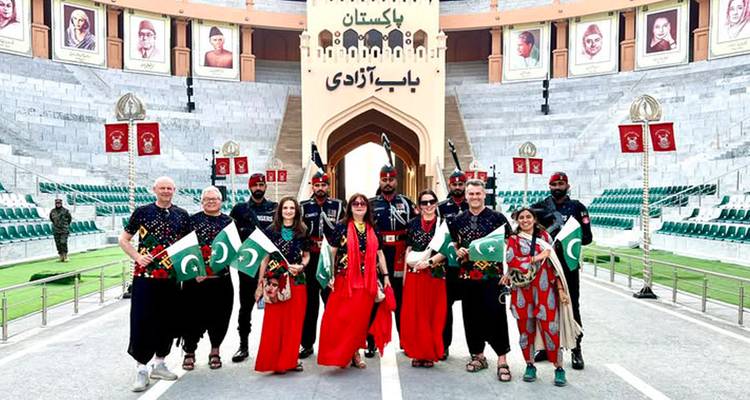 Group of travellers and soldiers wave Pakistani flags at the Wagah border ceremony gate.