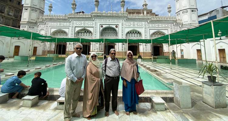 Une famille se tient pieds nus à côté de bassins turquoise devant une grande mosquée en marbre blanc.
