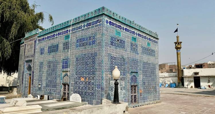 Un mausolée richement orné aux carreaux bleus se dresse sous un arbre feuillu au Pendjab.