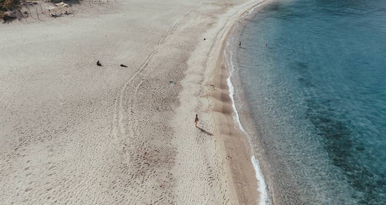 Vue aérienne d'une large plage de sable rencontrant une eau turquoise claire avec quelques visiteurs au loin.