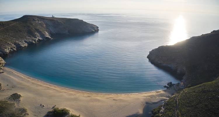 Vue aérienne d'une plage de sable en croissant et d'une baie turquoise calme au coucher du soleil avec le soleil se reflétant sur l'eau