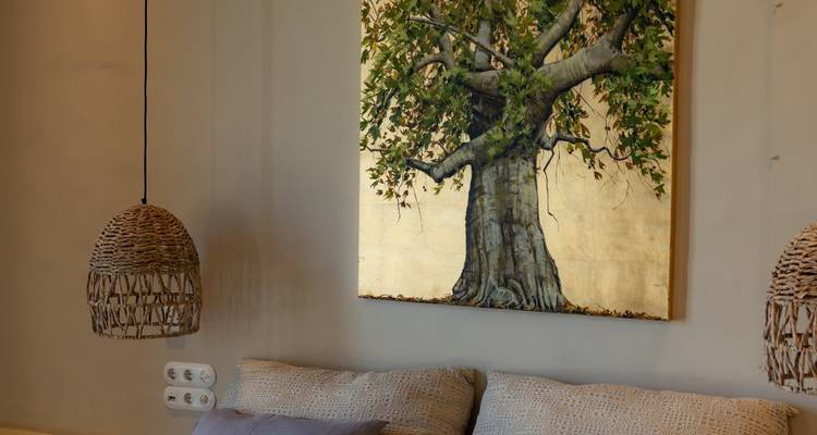 Détail intérieur d'une peinture d'un arbre sur fond doré avec des suspensions tressées au-dessus d'un canapé