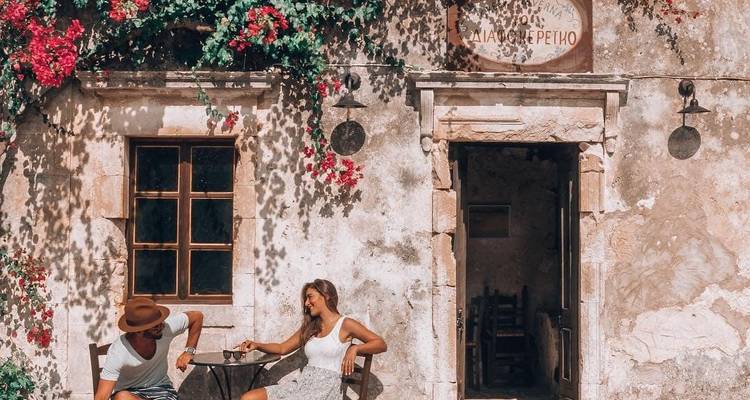 Jeune couple bavardant devant la façade pittoresque d'un café en pierre couverte de bougainvilliers