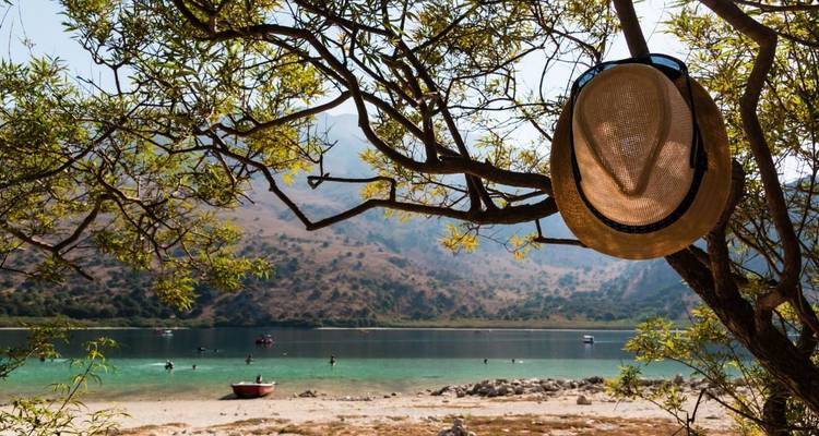 Chapeau de paille suspendu à une branche d'arbre surplombant un lac turquoise tranquille et des montagnes