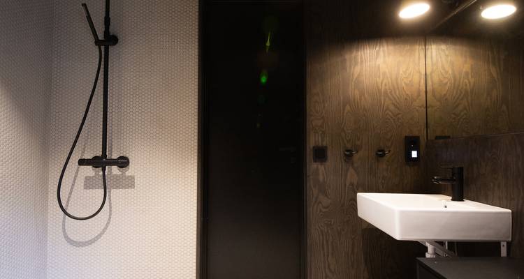 Baño minimalista con grifería negra, pared texturizada blanca y puerta de madera oscura