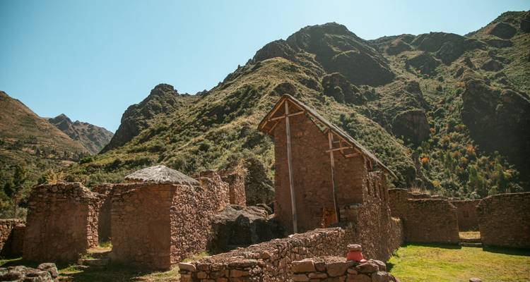 Stone walls of ancient Andean structures stand beneath rugged green slopes under bright daylight.