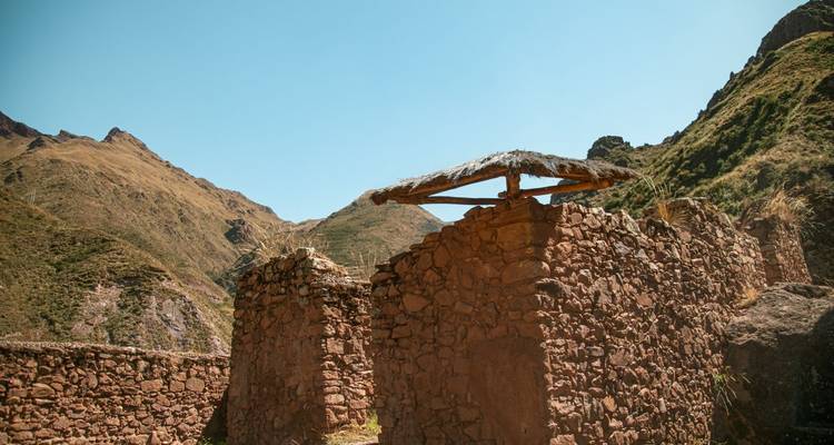 Close view of adobe-like Inca ruins with a thatched roof remnant set amid dry Andean hills.