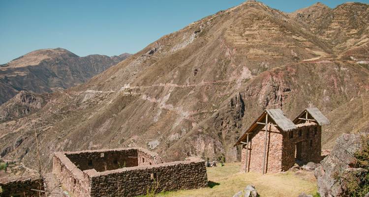 A stone house ruin overlooks a vast Andean valley and rugged mountain ridges under clear skies.