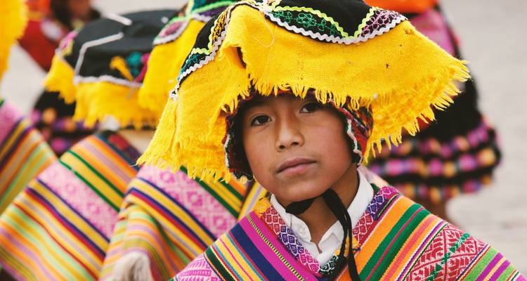 Junger peruanischer Junge trägt lebhafte traditionelle Festkleidung mit komplizierten gewebten Mustern und gelbem Hut.