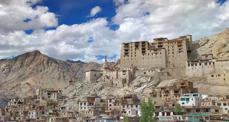 Der historische Leh-Palast und gestapelte weiß getünchte Häuser klammern sich an einen felsigen Himalaya-Hang unter blauem Himmel.