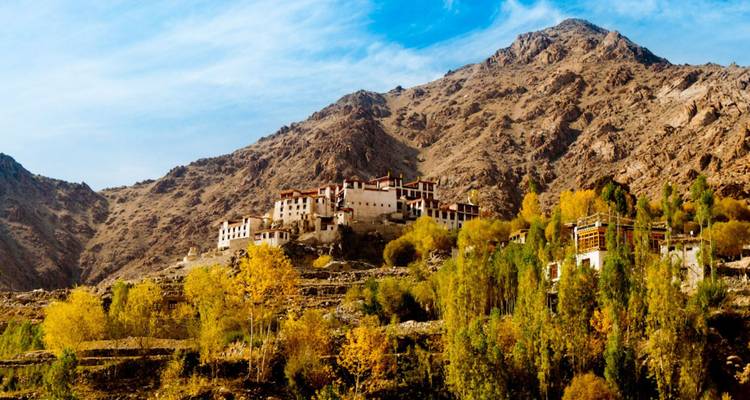 Ein abgelegenes Hilltop-Kloster überblickt herbstlich gefärbte Bäume und schroffe braune Klippen.