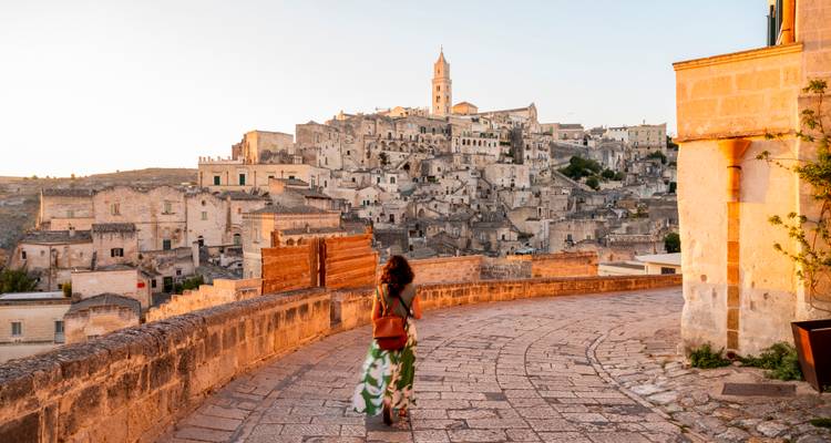 Frau, die entlang der sonnenbeschienenen Wehrgänge in Richtung der antiken Steinstadt Matera bei Sonnenuntergang spaziert