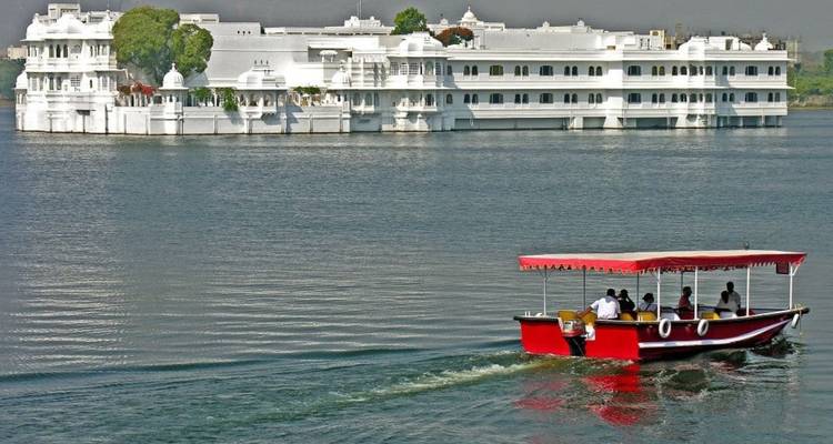 A red motorboat glides across Lake Pichola toward the gleaming white Taj Lake Palace.