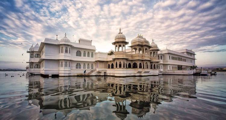 Majestic Lake Palace reflected in calm waters under a dramatic cloud-streaked sky.