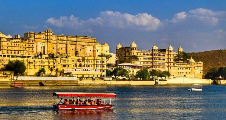 City Palace complex rises above the waters of Lake Pichola with a boat of tourists passing by.