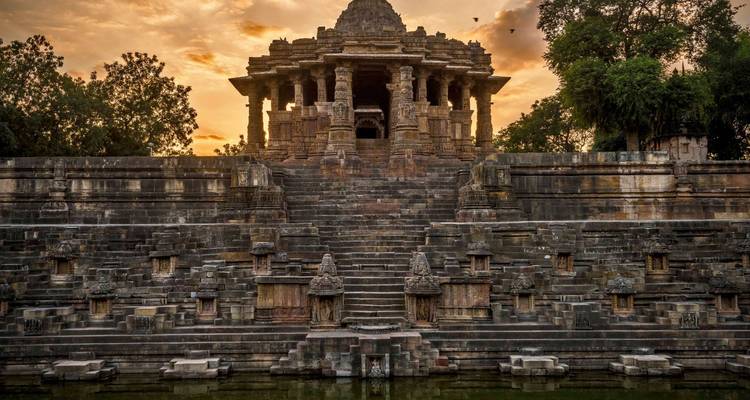 Modhera Zonnetempel trappen en sierlijke heiligdom gloeiend onder een dramatische zonsondergangshemel.