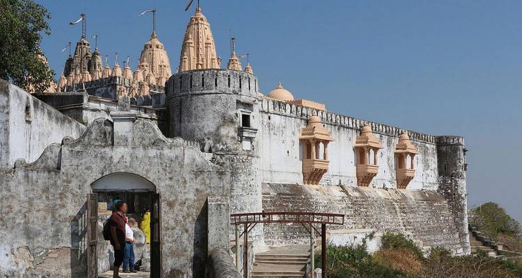 Bezoekers betreden de verweerde toegangspoort van Palitana's heuveltop Jain-complex onder gegroepeerde spitsen.