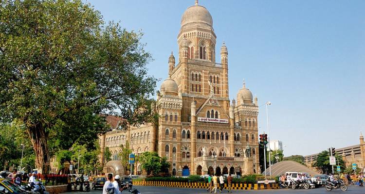 Drukke straatscène voor Mumbai's sierlijke BMC-gebouw onder een heldere blauwe hemel.