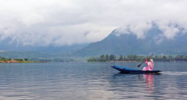 Femme en rose pagaie un petit esquif à travers le calme lac Dal avec des montagnes brumeuses au-delà.