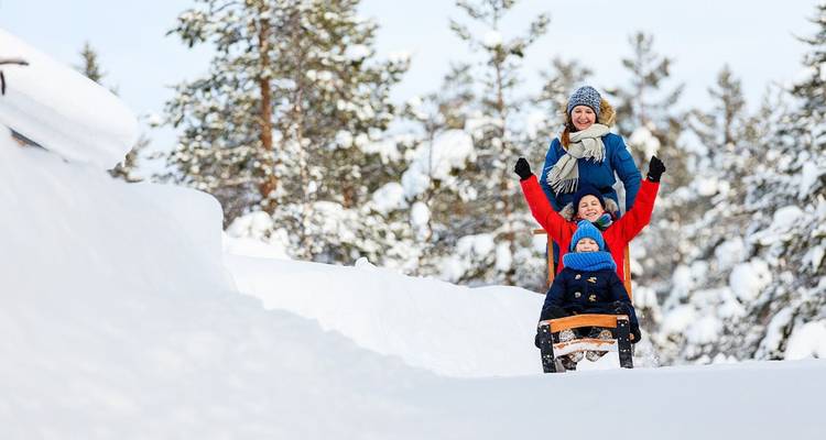 Mère et deux enfants dévalant joyeusement en luge un sentier forestier enneigé par une belle journée d'hiver.