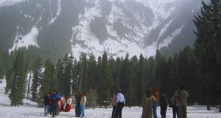 Les touristes se rassemblent dans une clairière enneigée au pied de montagnes escarpées couvertes de pins pour prendre des photos et jouer dans la neige.