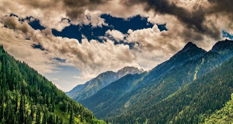 Ciel dramatique rempli de nuages au-dessus de crêtes montagneuses luxuriantes couvertes de pins.