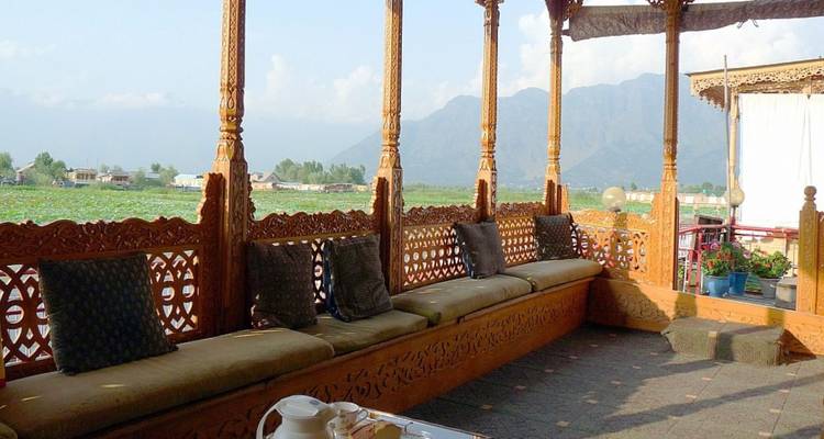 Geschnitzte Holzveranda eines Srinagar-Hausboots mit Blick auf einen lotusbedeckten See und entfernte Hügel.