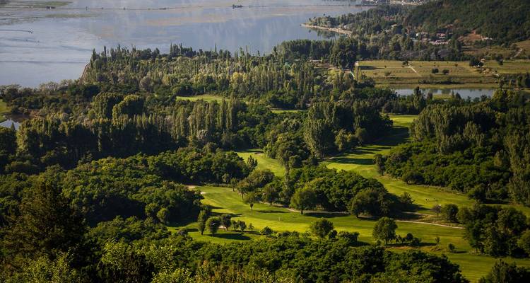 Luftaufnahme eines üppig grünen Golfplatzes und Wasserwege in der Nähe von Srinagar mit Bergen im Hintergrund.