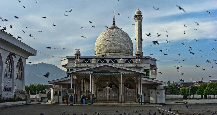 Weiß gekuppelte Moschee mit flatternden Tauben am Himmel und einigen Besuchern am Eingang.