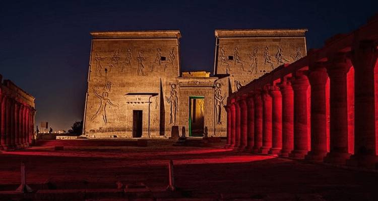 Espectáculo de luces nocturno proyectando tonos rojos sobre las columnatas del Templo de Filae bajo un cielo azul oscuro.