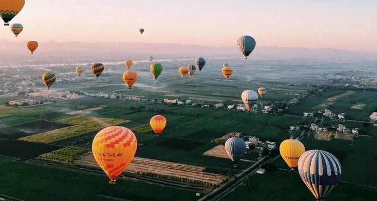 Docenas de globos aerostáticos coloridos flotando sobre campos fértiles y pueblos al amanecer en Luxor.