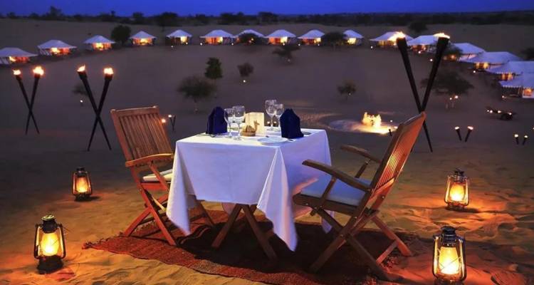 Cena romántica a la luz de velas montada entre dunas del desierto bajo el anochecer estrellado