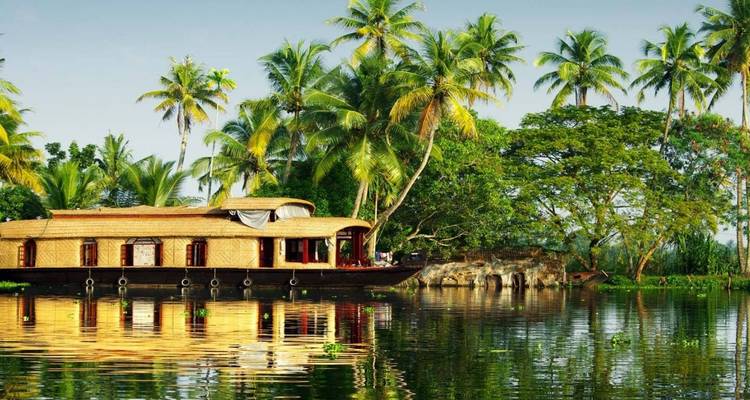 Péniche traditionnelle en bois se reflétant dans un lagon de backwater tranquille bordé de palmiers sous une lumière dorée