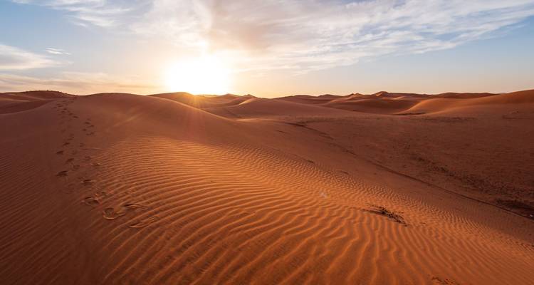Un coucher de soleil doré illumine les motifs ondulés des dunes s'étendant à travers un vaste paysage désertique.