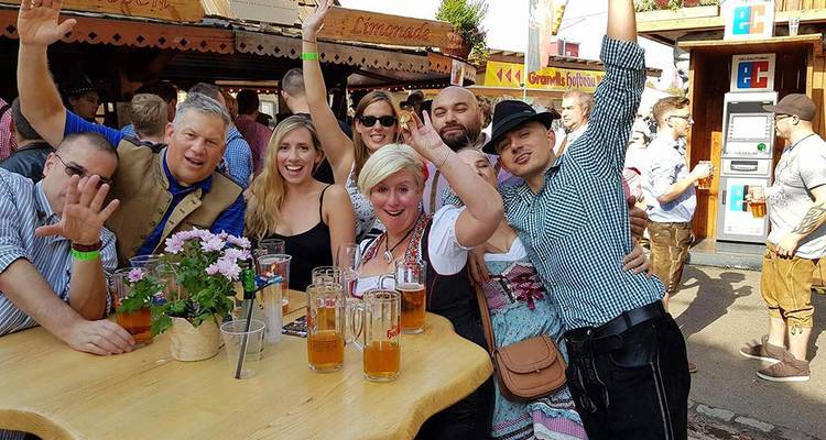 Vrolijke vrienden die bieren heffen rond een houten tafel op een buitenfestival in Beieren.