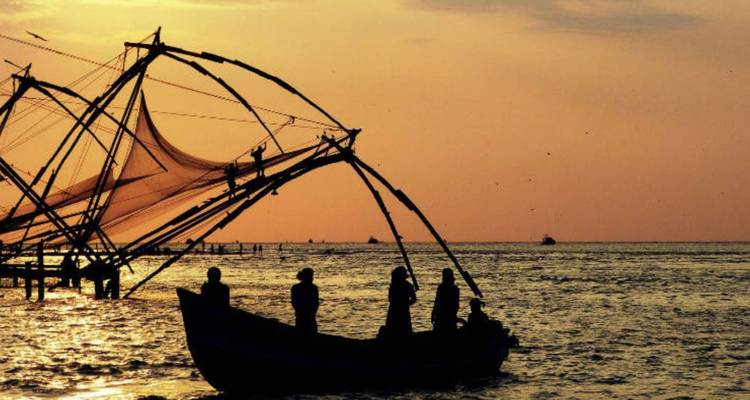 Silhouettierte Fischer und ikonische chinesische Fischernetze vor einem orangefarbenen Sonnenuntergangsmeer