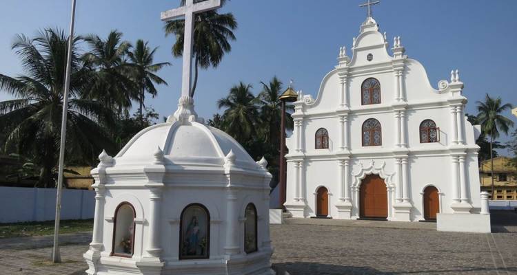 Weiße Kolonialkirche mit Kreuz und Palmen unter strahlend blauem Himmel
